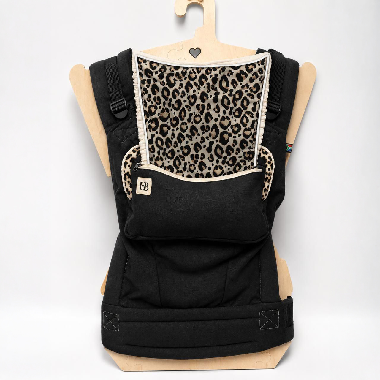Black baby carrier with leopard-print lining and front pocket, displayed on a wooden hanger.